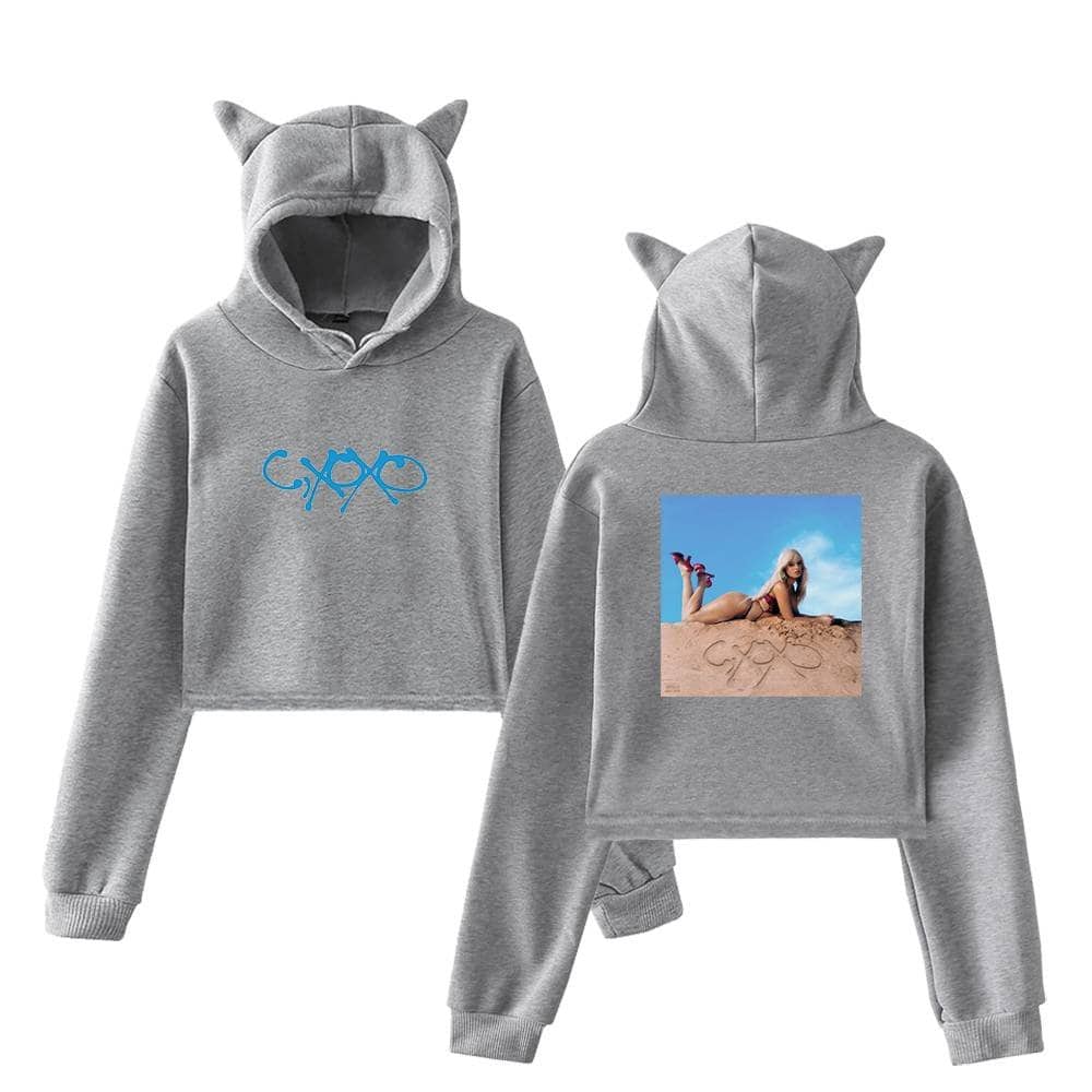 Grey cropped hoodie with cat ears, front blue logo design, back picture of a woman lying on sand with sunglasses and red shoes, casual streetwear for women, latest trendy apparel for casual outings and comfortable fashion.