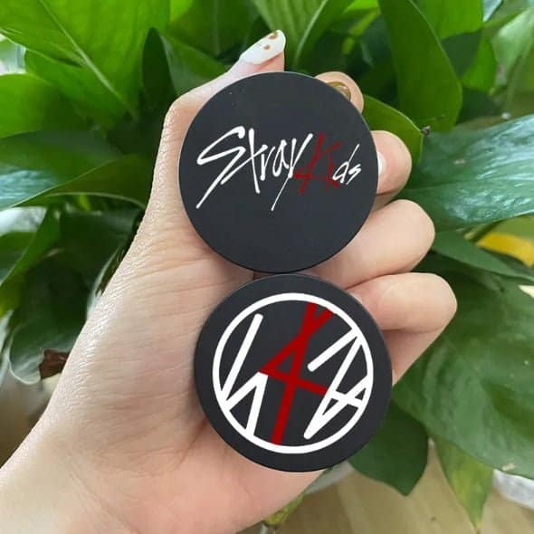 Black circular patches with stylish printed designs, held in a person's hand against a backdrop of green leaves.